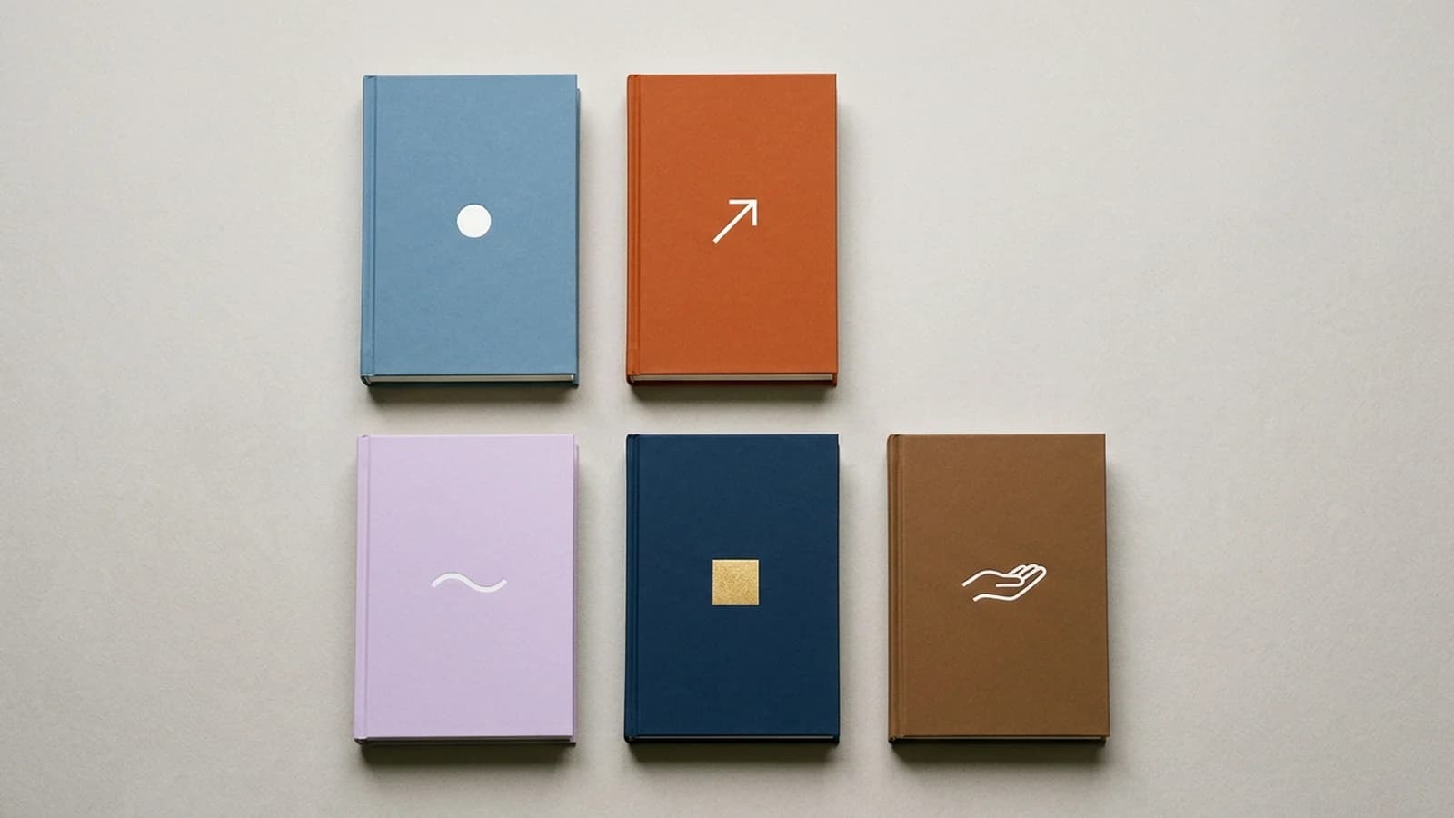 A grid of five matte hardcover self-help books in five different sub-genre palettes: dusty blue with a circle, burnt orange with an arrow, soft lavender with a wave, deep navy with a gold square, warm umber with an open hand